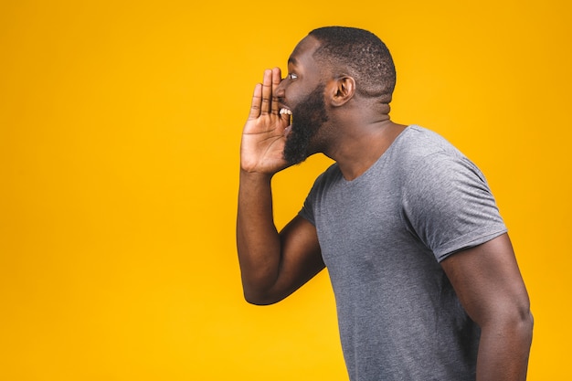 Side view portrait of a young african american man screaming out loud with hand at his mouth isolated on the yellow wall