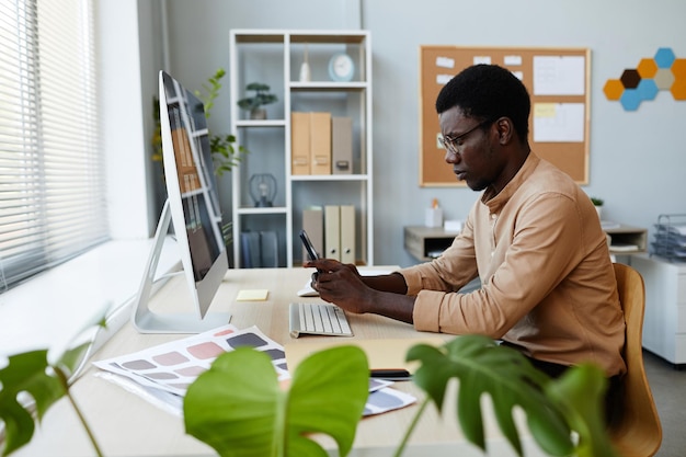 Side view portrait of young black man using smartphone at
workplace in minimal office setting with p