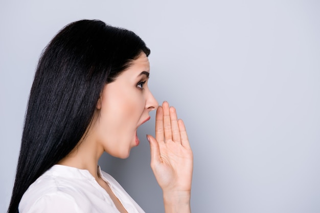 Side view portrait of young charming woman holding her hand near the mouth and telling about interesting news