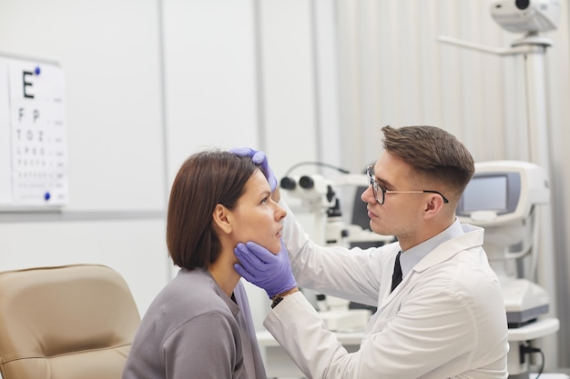 Side view portrait of young ophthalmologist opening eye of female patient