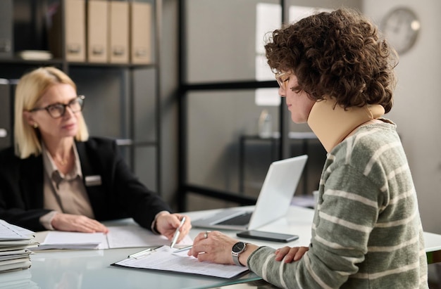 side view portrait of young woman with neck injury filling documents at insurance agency