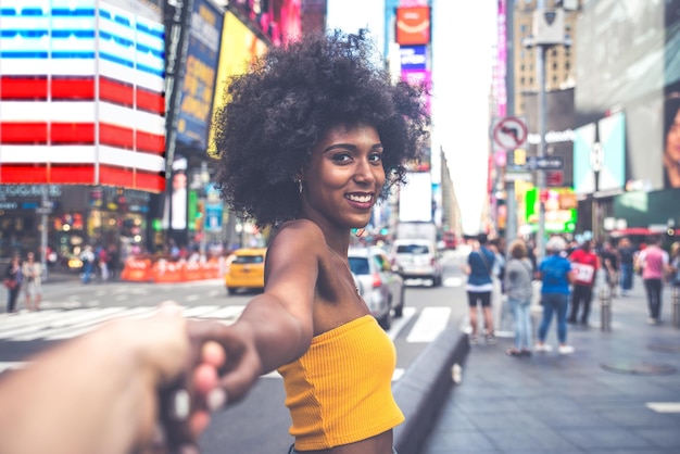 Side view portret van een gelukkige jonge vrouw met een afro kapsel die de hand vasthoudt op een stadsstraat
