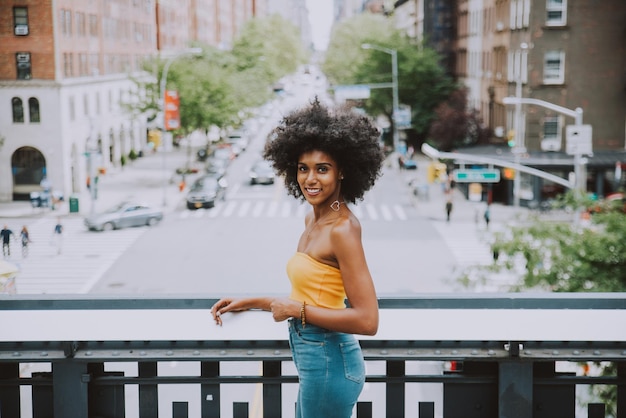 Side view portret van een zelfverzekerde jonge vrouw met een afro kapsel die op een brug tegen een stadsstraat staat