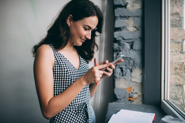 Side view of positive Caucasian female student in casual apparel using cellphone application