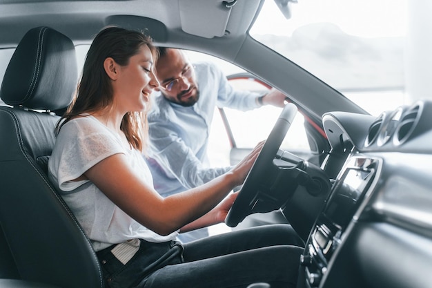 Vista laterale di una ragazza positiva che ha una visita in autosalon e sceglie il manager dell'auto che l'aiuta