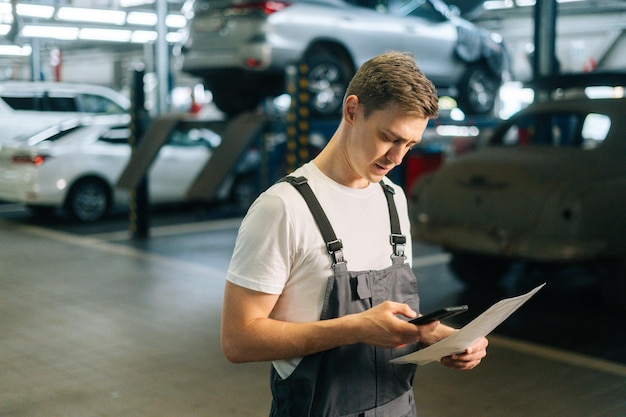 Side view of professional handsome young mechanic male wearing uniform holding clipboard and using