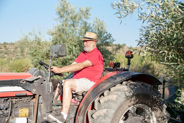 Foto vista laterale di un orgoglioso agricoltore più anziano con un cappello che lavora nel campo con un trattore