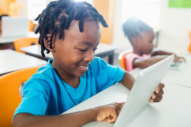 Photo side view of pupil using tablet pc in classroom