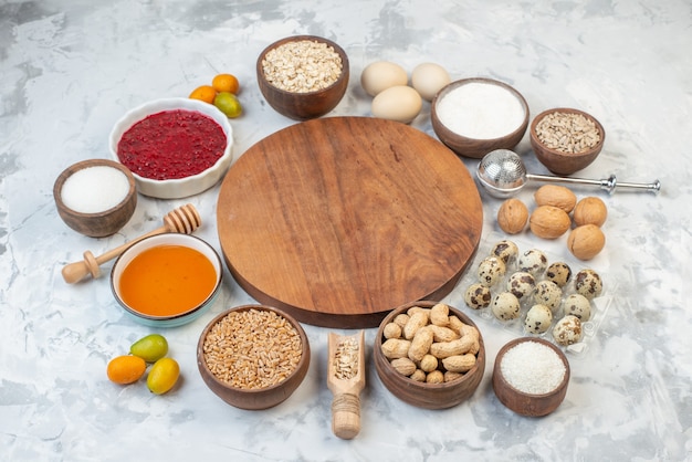 Side view of round wooden board among flour jam dried fruits fresh kumquats eggs brown rice on ice background