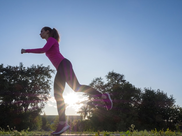 Side view of a running woman in city park area during sunset.