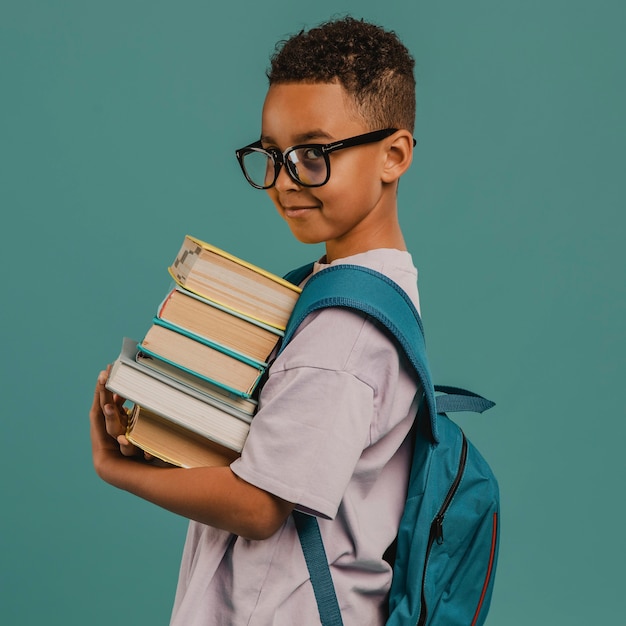 Photo side view school boy holding a pile of books