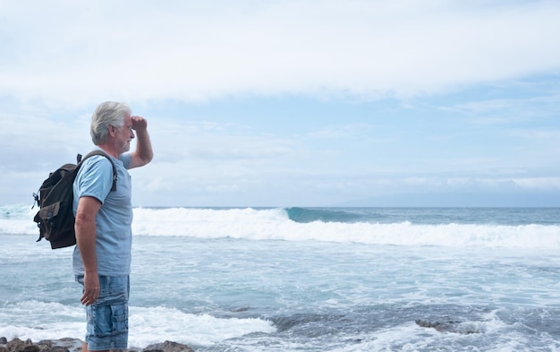 Photo side view of senior backpack man standing at beach