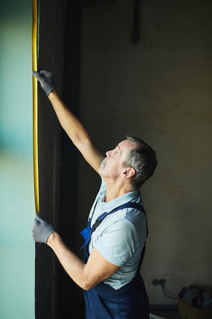 집, 복사 공간을 리노베이션하는 동안 테이프로 벽을 측정하는 수석 건설 노동자의 측면보기