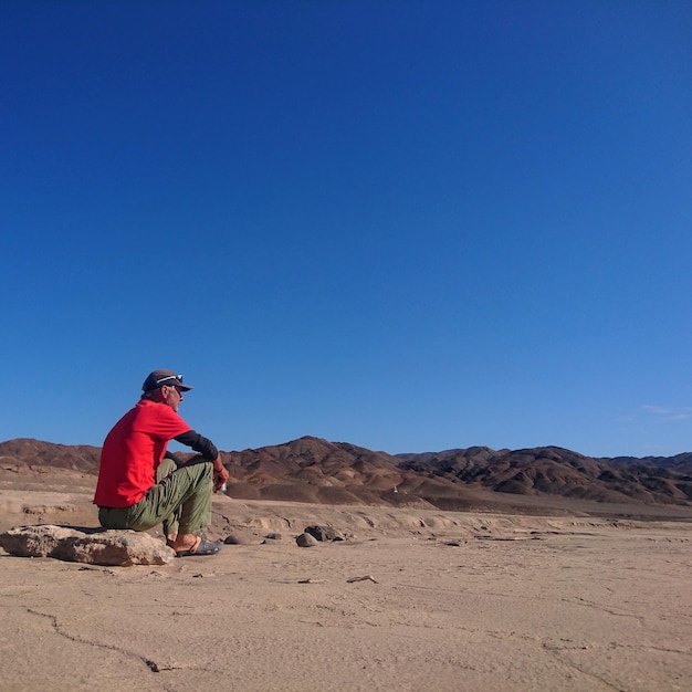 Side view of senior man sitting on field against clear blue sky