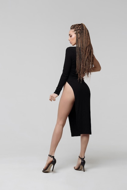 Side view of sensual young female with long dreadlocks wearing amazing black dress