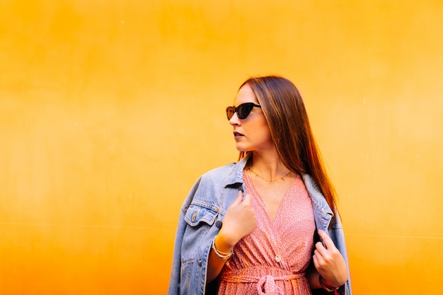 Side view of serious elegant woman in casual pink dress, denim jacket and blue eye cat sunglasses looking calm and confident.