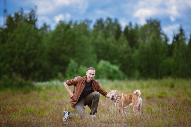 畑を散歩している飼い主とシャーペイ犬の側面図。緑の草と青い曇り空