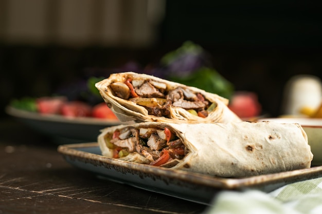 Photo side view shawarma rolls in plate on wooden table