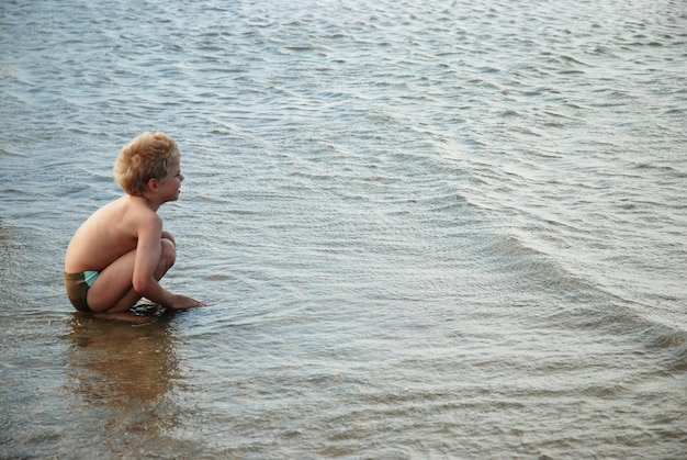 Side view of shirtless boy crouching at beach