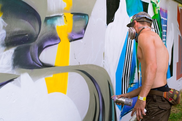 Photo side view of shirtless street artist painting graffiti on wall