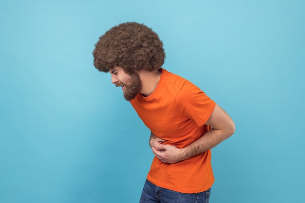 Side view of sick sad unhealthy man with Afro hairstyle standing and holding his painful belly