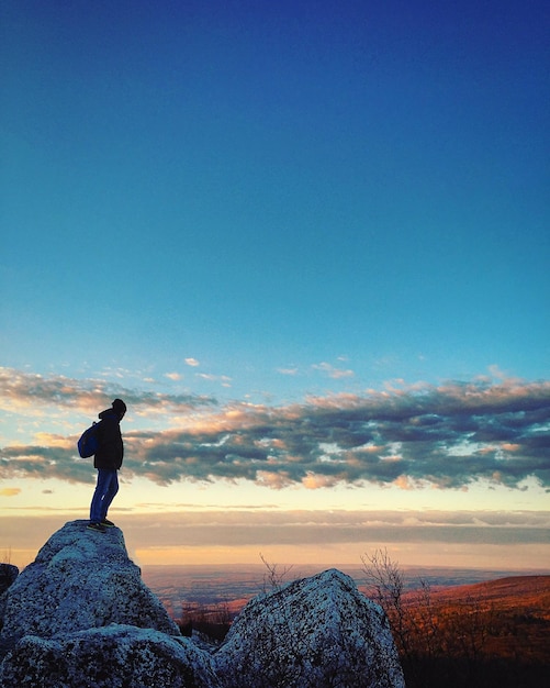 Side view of silhouette man standing on cliff at sunset