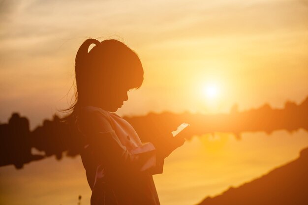 Side view of silhouette woman using smart phone against sunset sky