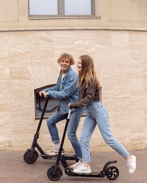 Photo side view of smiley couple using electric scooters in the city