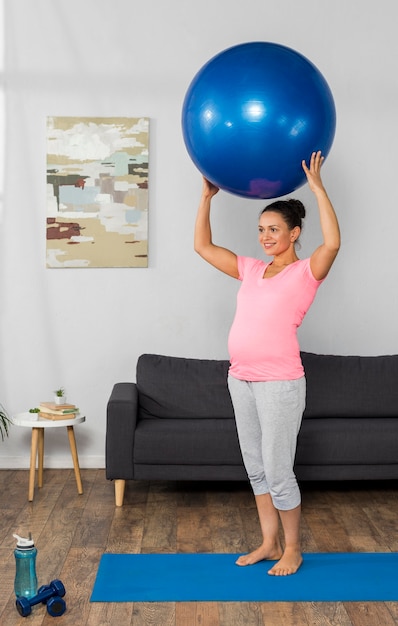 Foto vista laterale della donna incinta di smiley a casa formazione con la palla sulla stuoia