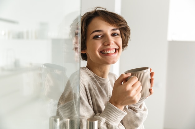 家でコーヒーを飲む笑顔のブルネットの女性の側面図