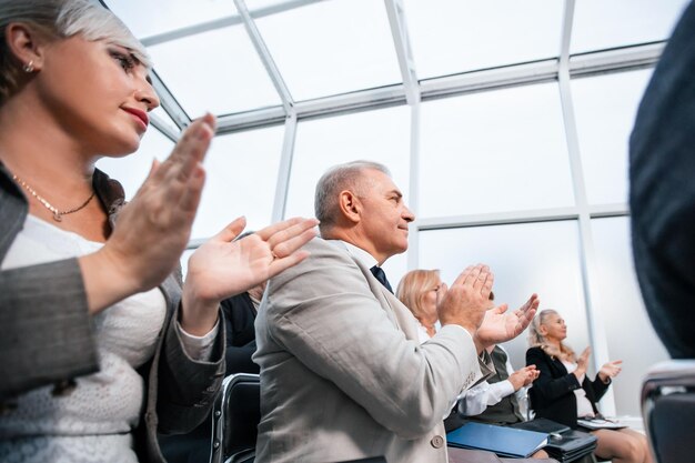 Foto vista laterale. ascoltatori di seminario di affari sorridenti che applaudono insieme. affari e istruzione