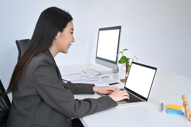 Вид сбоку улыбающаяся деловая женщина, работающая с ноутбуком на своем рабочем месте.