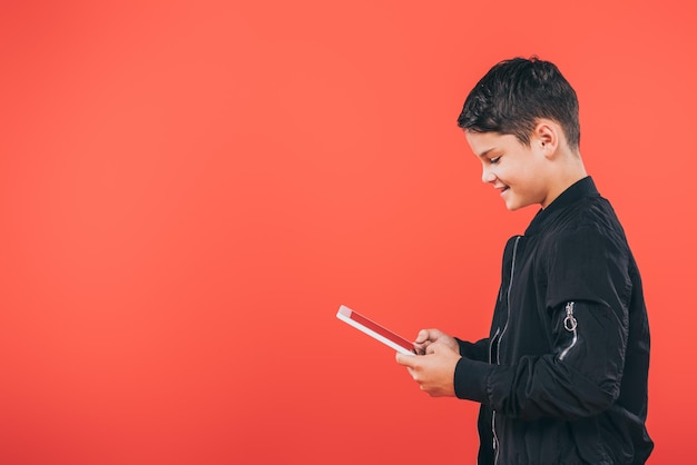 Side view of smiling child using digital tablet isolated on red