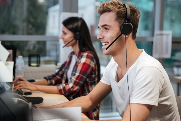 Side view of Smiling Coworkers sit by the table in headphones. Call center