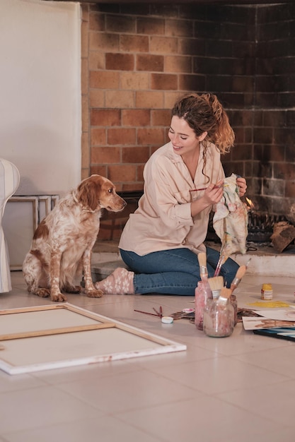 Side view of smiling female artist bonding with pet while drawing using professional paints in creative workspace