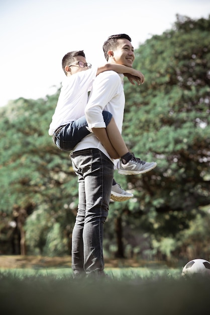 Side view of smiling man giving son piggyback at park