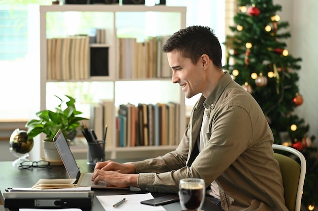 Вид сбоку улыбающийся мужчина, работающий с ноутбуком дома