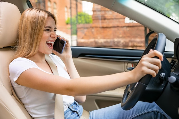 車を運転し、スマートフォンで話している笑顔の女性の側面図