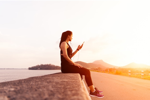 Side view of sport woman with earphones sitting on the wall after afternoon run.