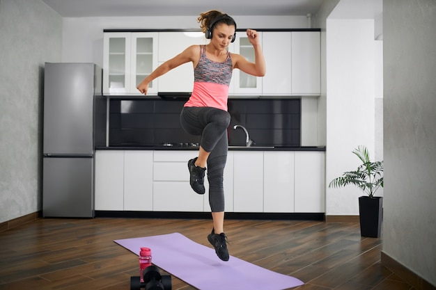 Side view of strong young woman jumping on mat in kitchen.