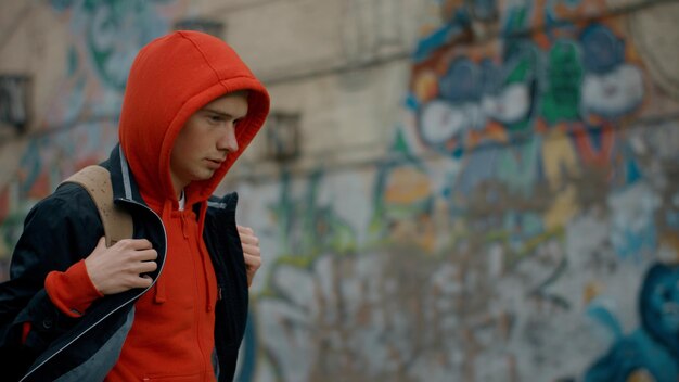 Side view of student boy in red hoodie walk in city