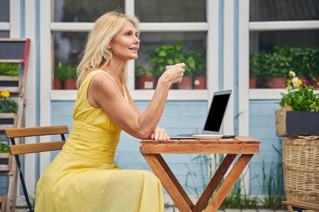 Side view of a stylish thoughtful middle-aged blonde Caucasian woman sitting at a wooden table