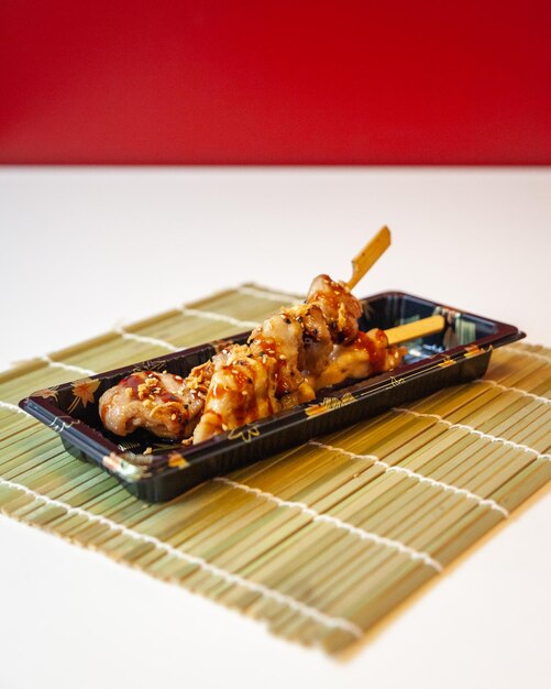 Side view of take away Japanese yakitori skewers on a bamboo mat on white table and red background with copy space