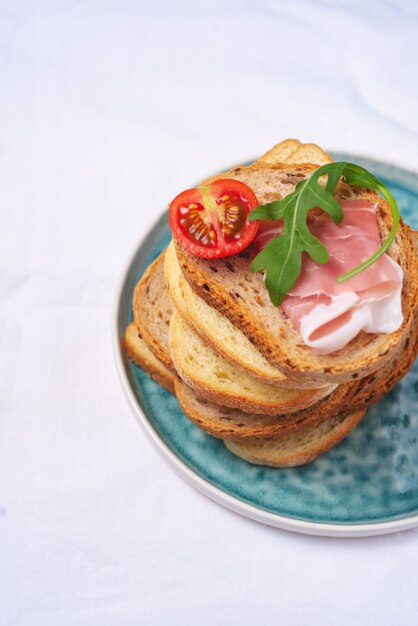 Side view, tasty fresh pieces of bread with ham tomatoes and rocket salad 