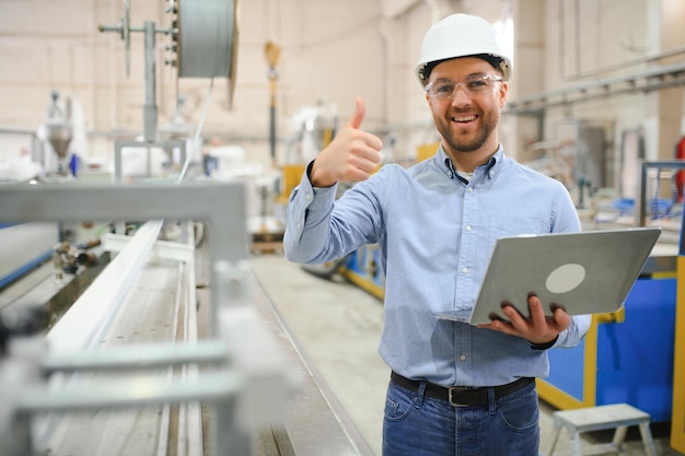 Foto vista laterale di un tecnico o un ingegnere con cuffie e portatile in piedi in una fabbrica industriale