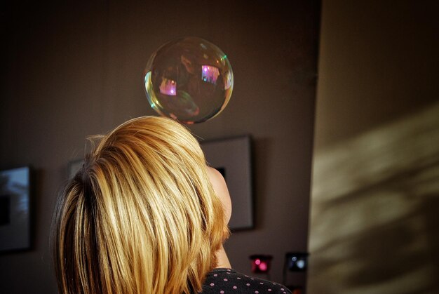 Photo side view of teenage girl playing with bubble at home