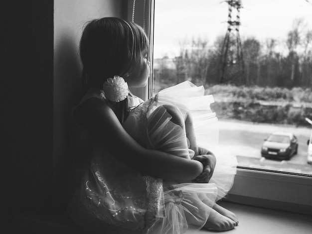 Photo side view of thoughtful girl looking through window at home