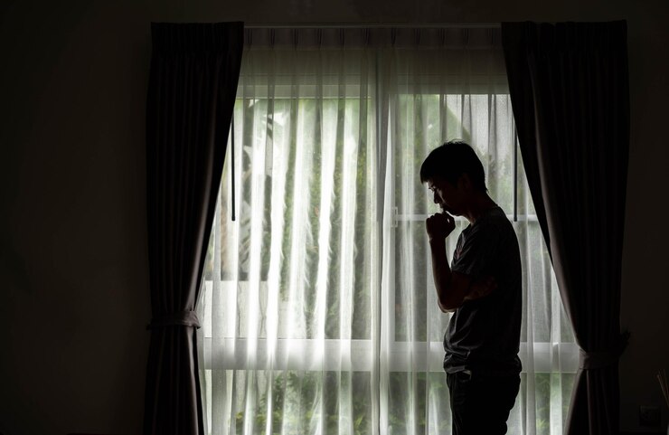 फोटो side view of thoughtful man standing by window at home