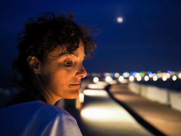 Vista laterale di una donna pensierosa che guarda lontano di notte