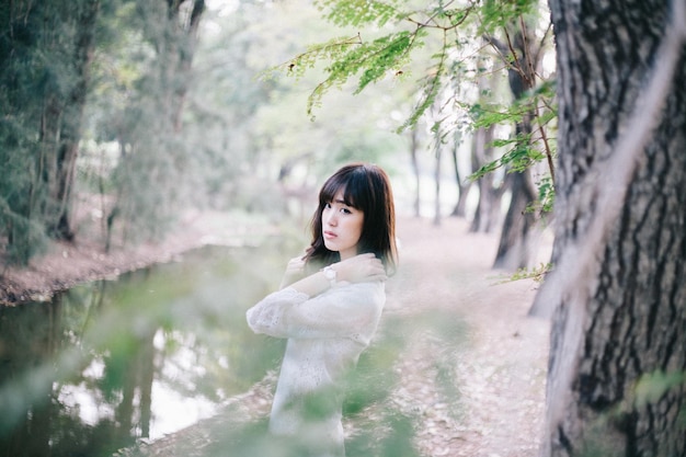 Side view of thoughtful young woman standing at stream in forest